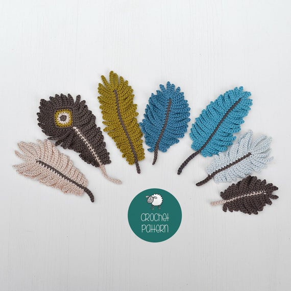 Seven crochet feather appliqués in brown, green, blue, beige, and gray yarn are arranged in a semicircle on a white surface, with a circular tag labeled CROCHET PATTERN at the center bottom.