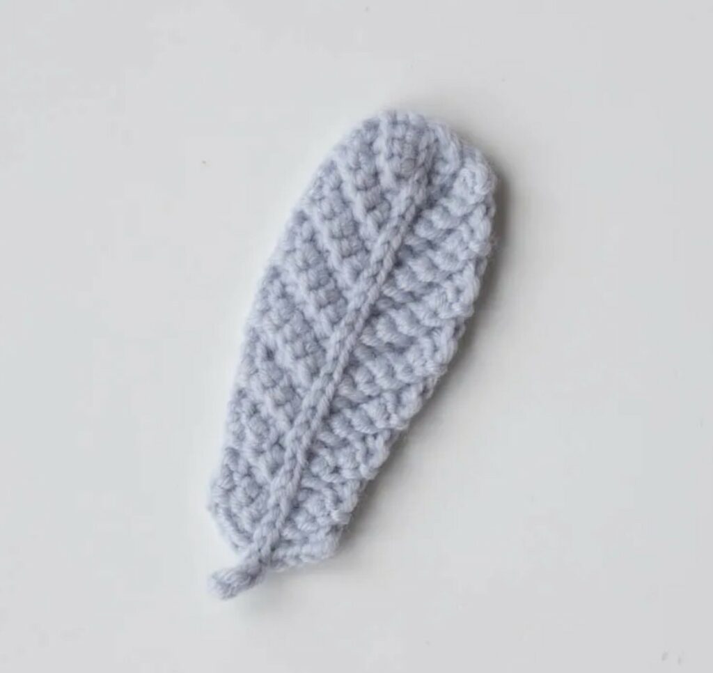 A single light gray crochet feather with a textured, ribbed pattern is displayed on a plain white background.