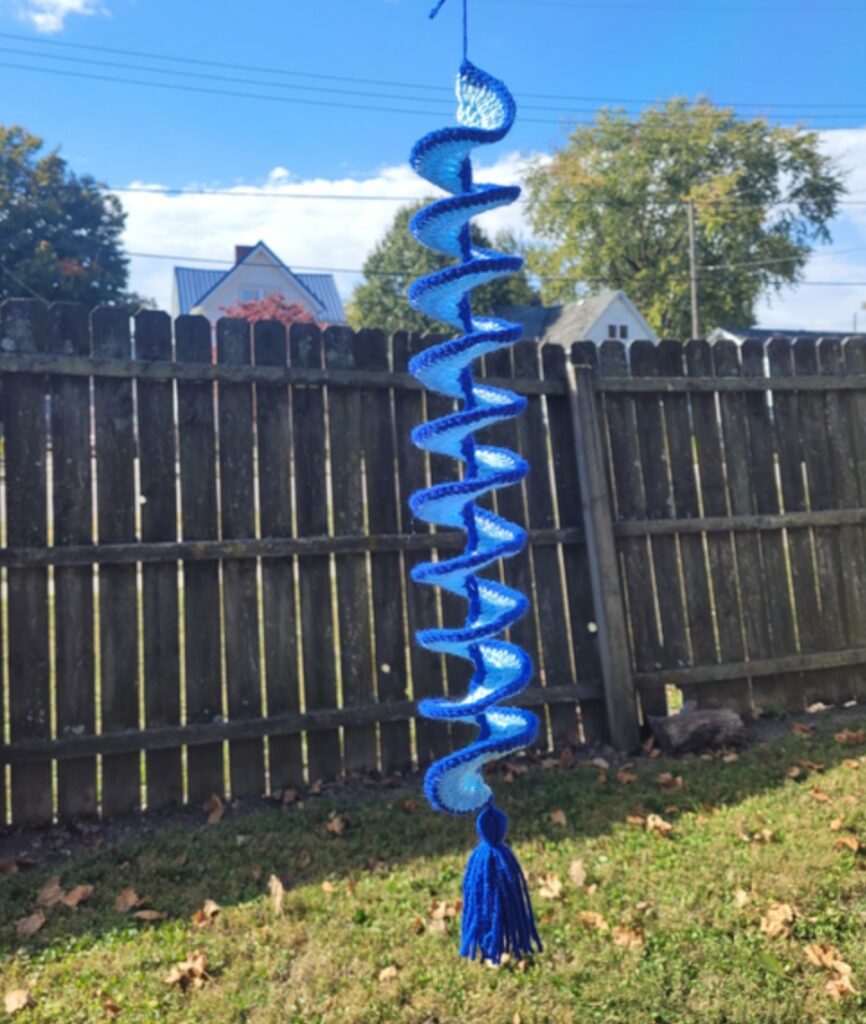 Multiple handmade crochet wind spinners spinning outdoors, showcasing their spiral shapes.