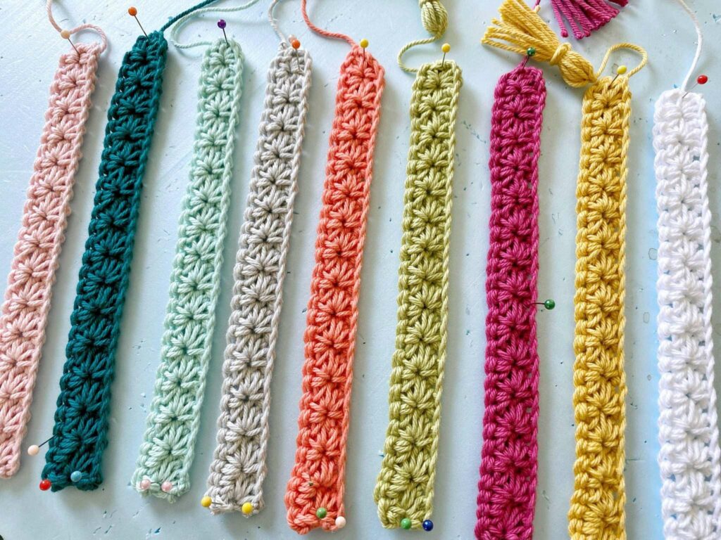 Ten crocheted bookmarks in various colors are pinned side by side on a flat surface, each displaying a textured pattern and a loop or tassel at one end—perfect for back-to-school crochet or September cozy crochet project ideas.