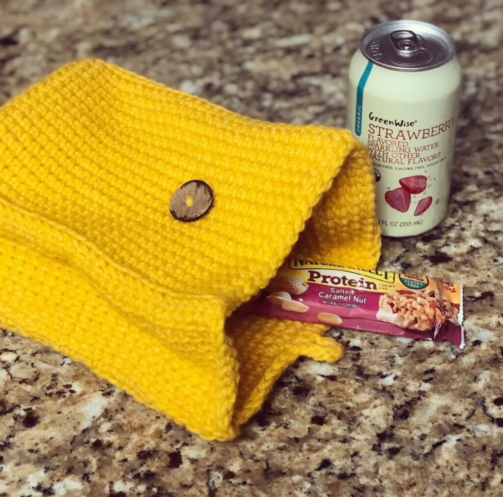 A yellow knitted pouch, a can of strawberry sparkling water, and a salted caramel nut protein bar on a granite countertop—perfect inspiration for September cozy crochet project ideas.