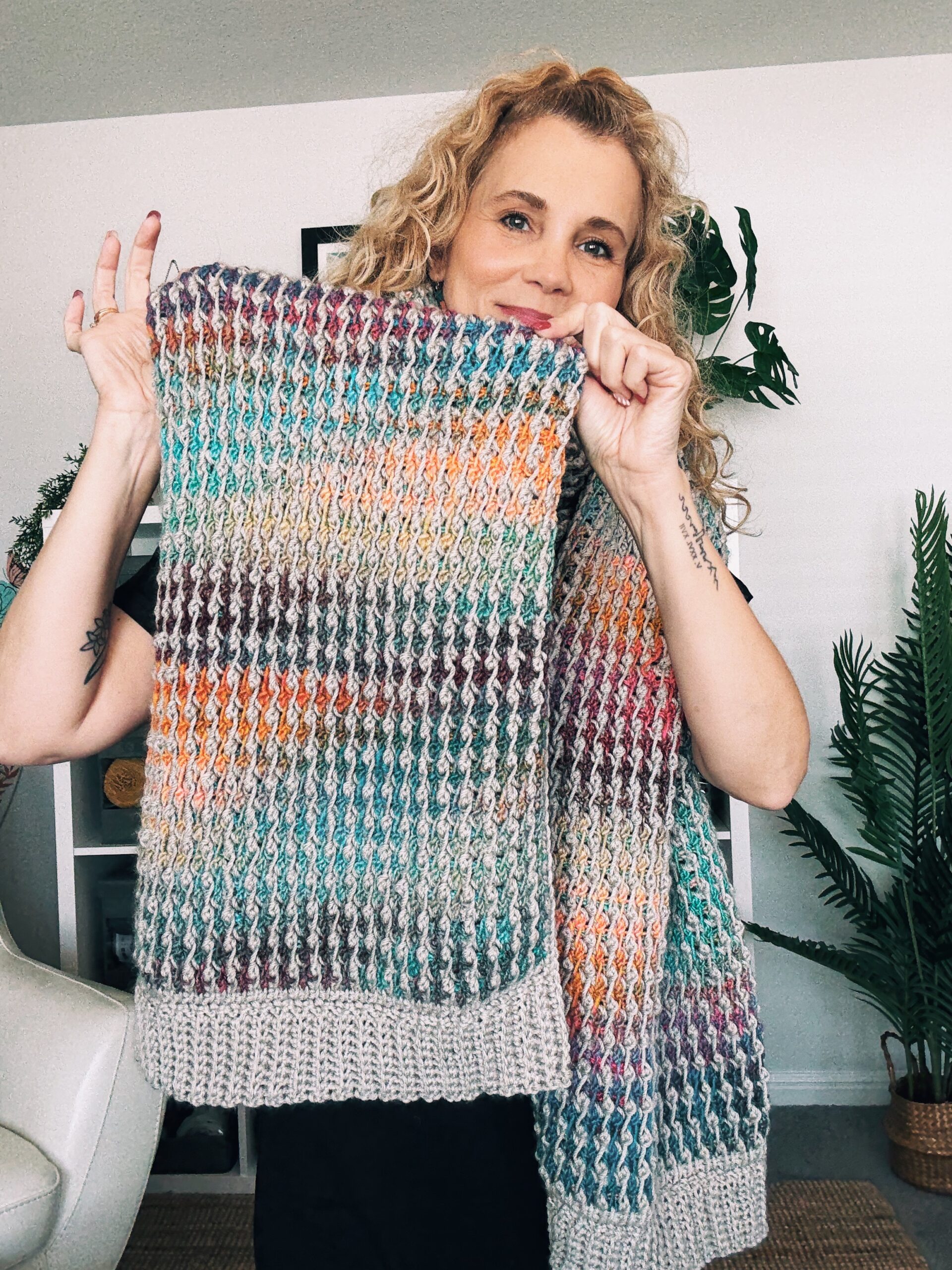 Model wrapped in a Tunisian crochet blanket scarf created with the field stitch in gray and colorful yarn stripes.