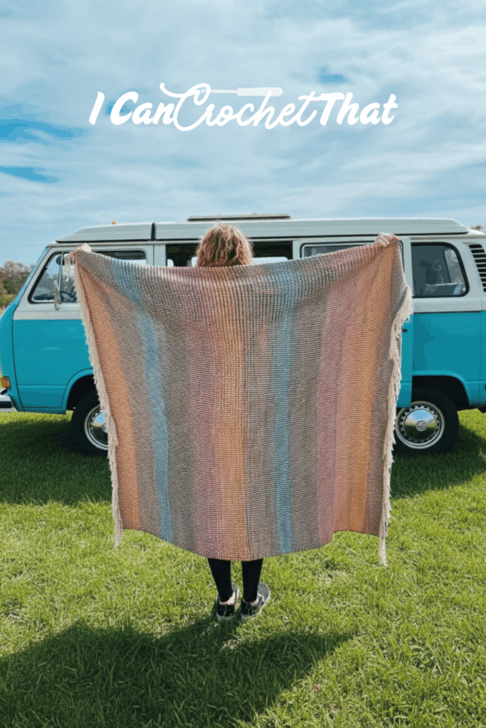 A person standing on grass holds up a pastel-striped crocheted blanket in front of a blue van. The text I Can Crochet That appears at the top.