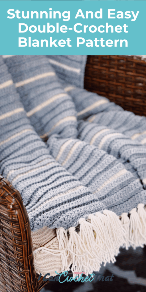 A blue and white striped double-crochet blanket with fringe is draped over a brown wicker chair.