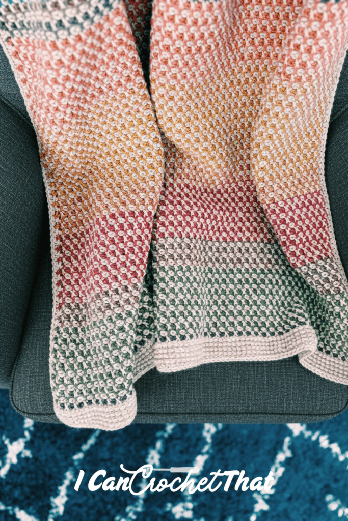 A multicolored crocheted blanket with pink, yellow, and green sections is draped over a dark gray armchair. The text I Can Crochet That appears at the bottom.