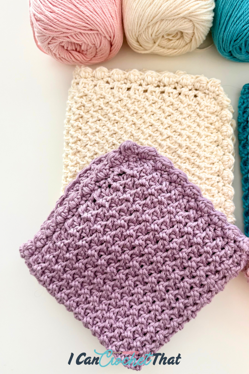 Two crocheted square swatches, one purple and one cream, are displayed on a white surface with pink, cream, and teal yarn balls above them.