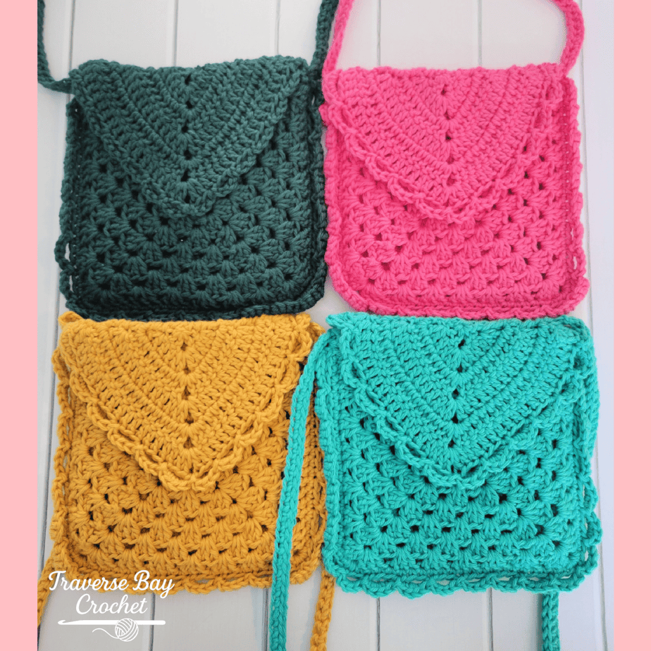 Four crocheted purses in dark green, pink, yellow, and teal are arranged in a square on a white surface. Each purse has a flap closure and a shoulder strap.