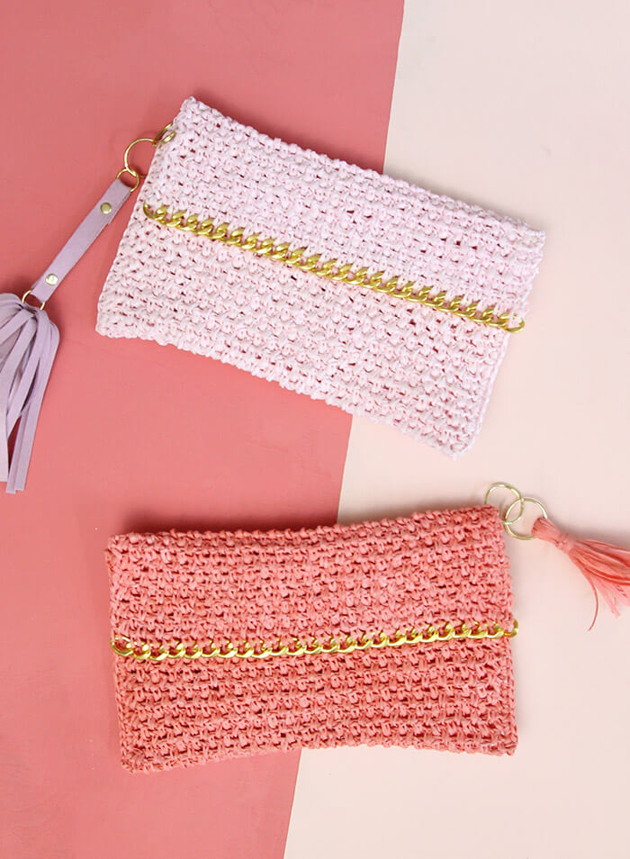 Two crocheted clutch bags, one pink and one coral, each with a gold chain accent and a matching tassel keychain, displayed on a pink and cream background.