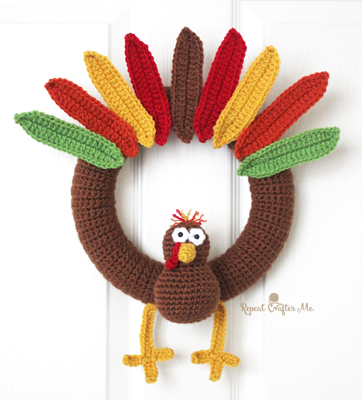 A crocheted turkey wreath with colorful feathers in red, yellow, and green, hanging on a white door.