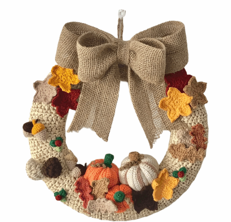 A decorative wreath with crochet leaves, acorns, pumpkins, and a large burlap bow on top, featuring autumn colors.