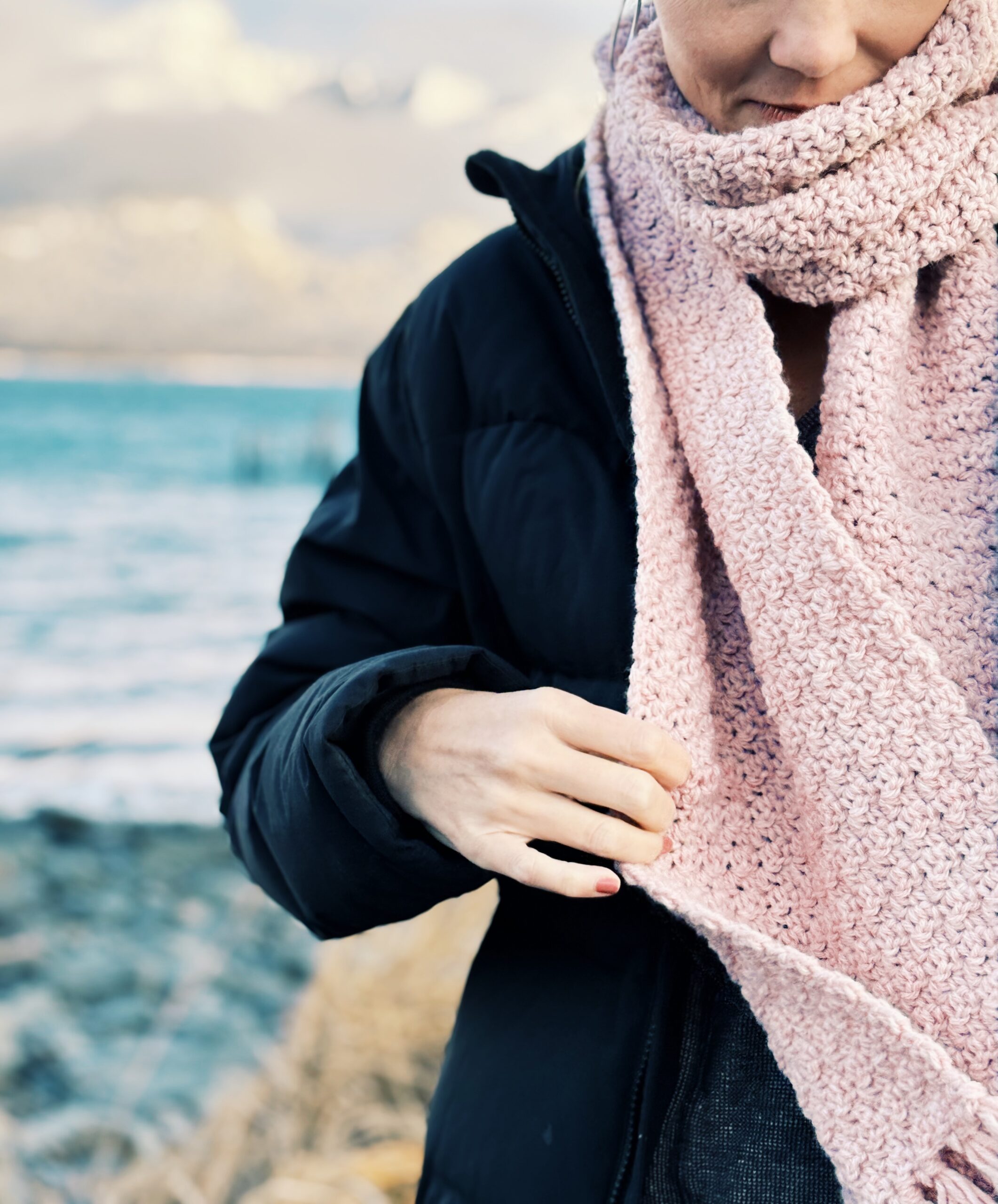 A person in a black puffer jacket wearing a large, textured pink scarf.