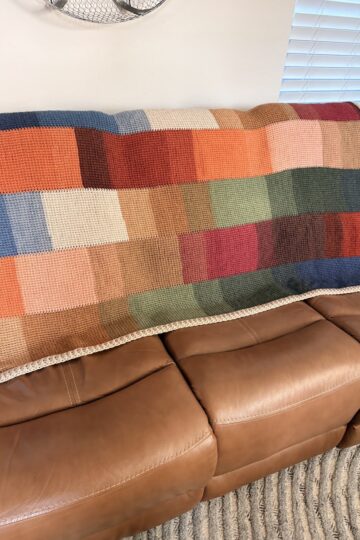 Crocheted patchwork blanket made of multicolored squares draped over a brown leather couch.