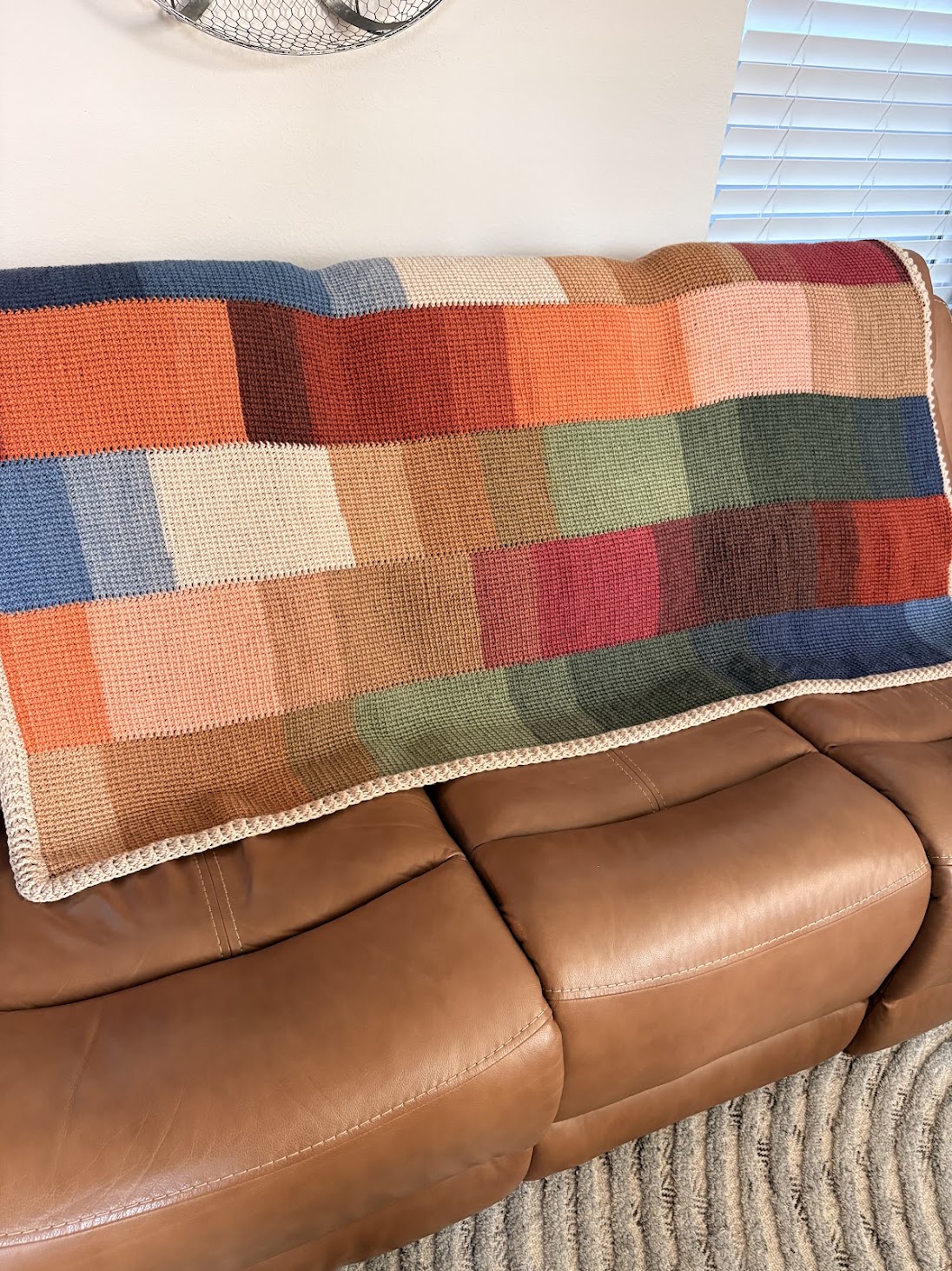 Crocheted patchwork blanket made of multicolored squares draped over a brown leather couch.